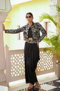 Woman in a stylish outfit with a patterned jacket and black pants standing in a decorative indoor setting.
